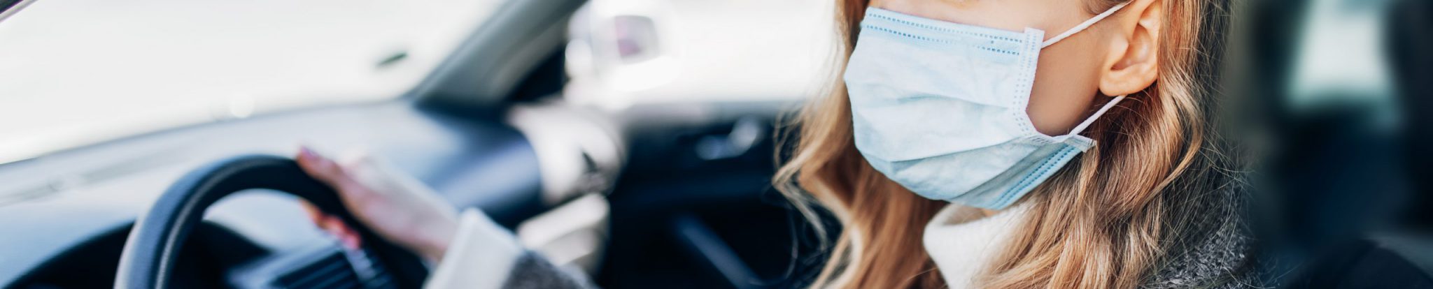 A woman wearing a medical facemask in her car during the COVID-19 pandemic.