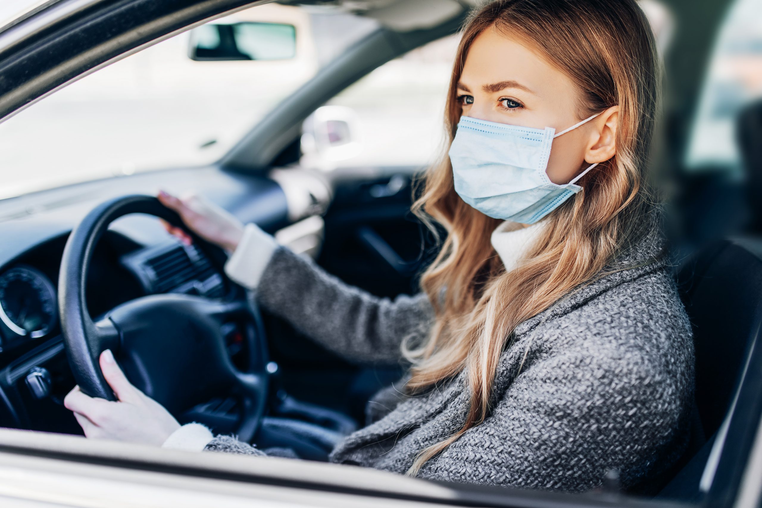 A woman wearing a surgical face mask while driving during the COVID-19 pandemic.