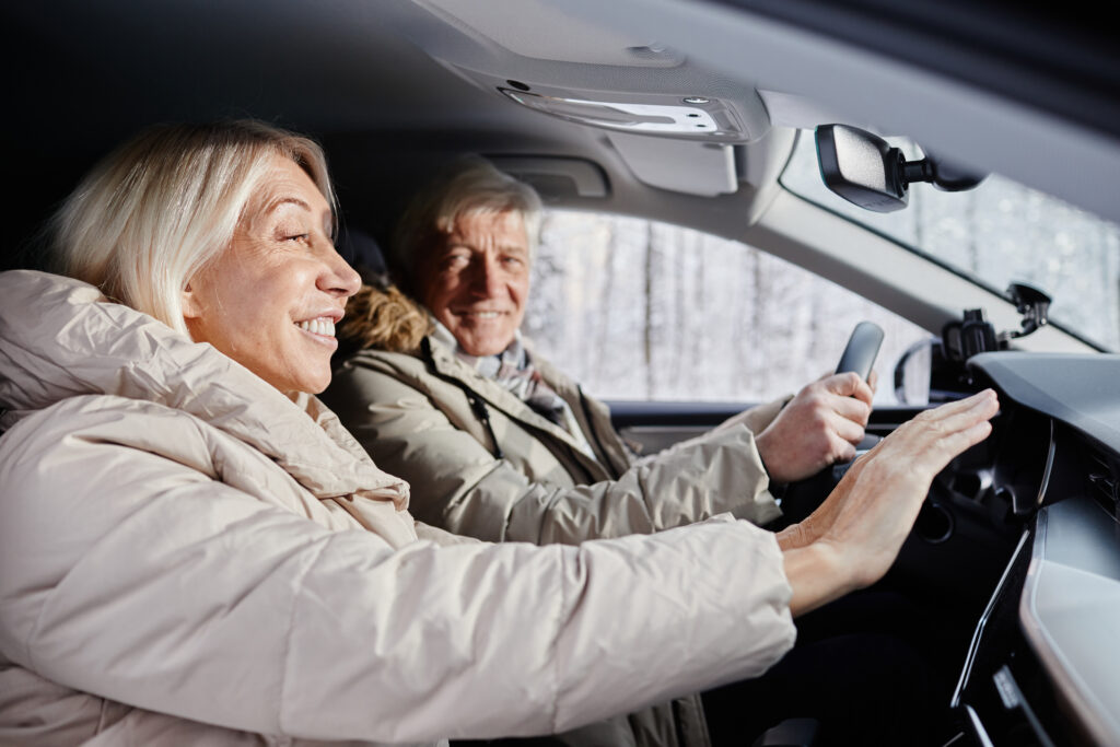 Older couple warming up inside a car during winter, adjusting the car’s heater.