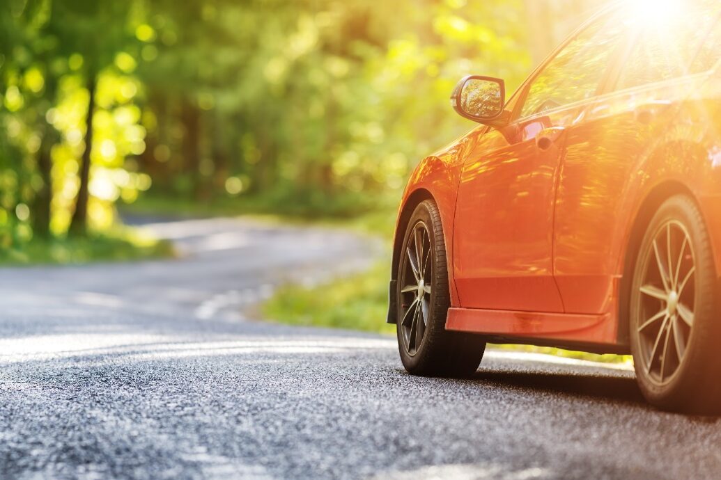 Red car driving along a winding road surrounded by spring greenery